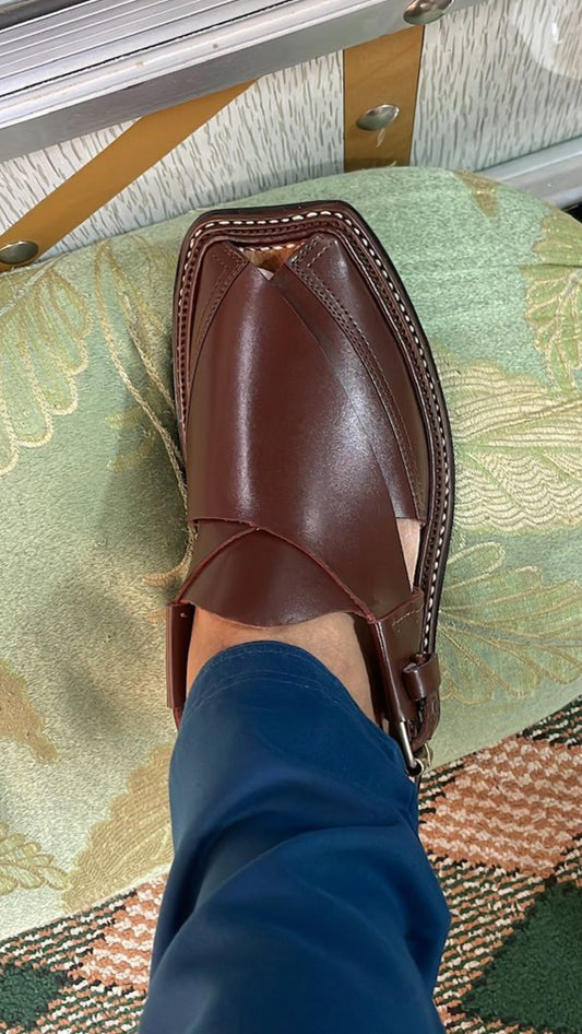 Brown leather shoe on a patterned rug with a blue sock.